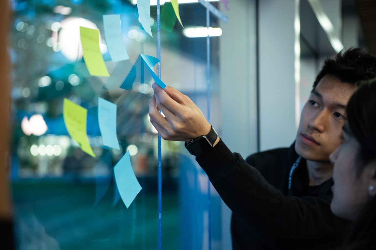 colleague works with teammate to put post-it notes on window.